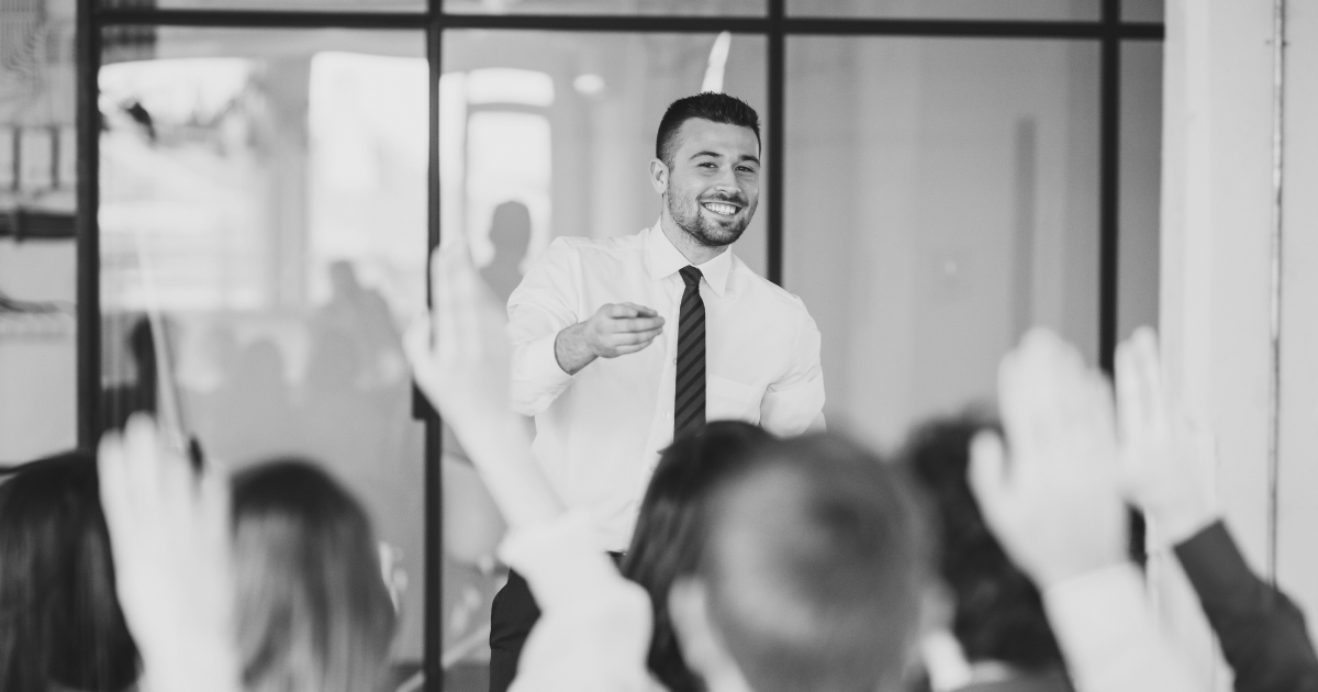 A man in formal attire educates sales team, using visual aids to enhance his message to the audience.