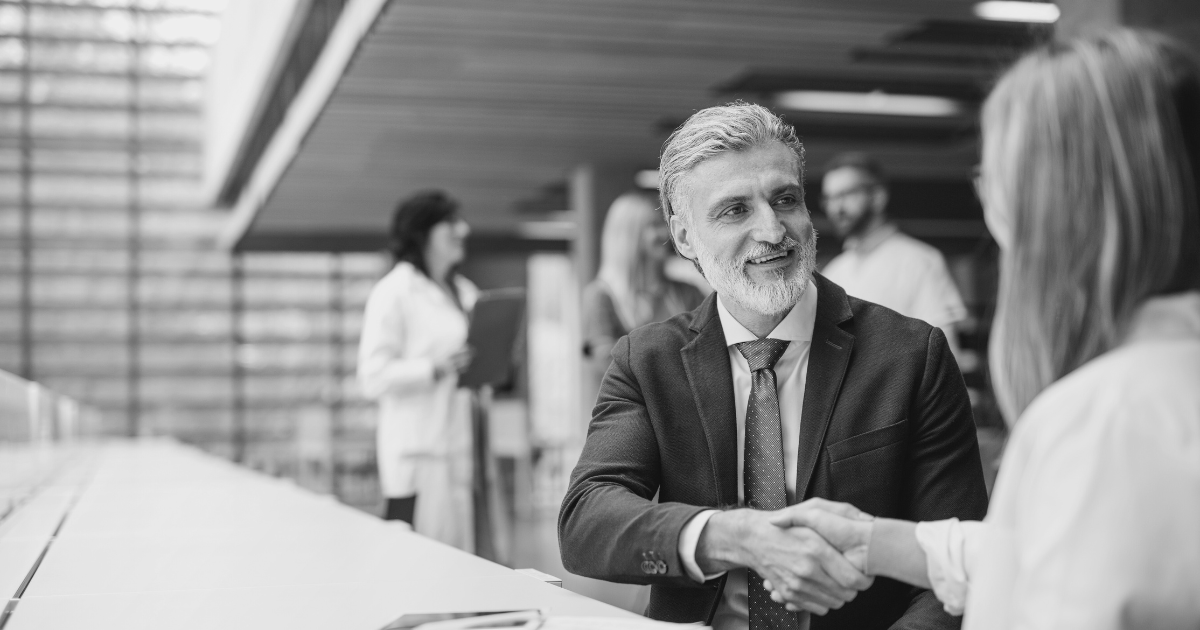 A man and woman in an office shaking hands, indicating the completion of a sales agreement.